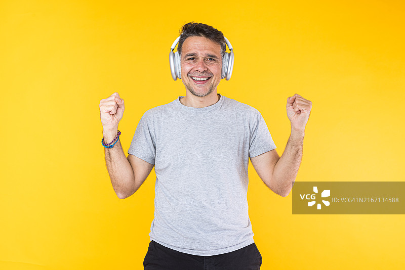 戴着降噪耳机，在黄色背景上享受音乐的微笑男人图片素材