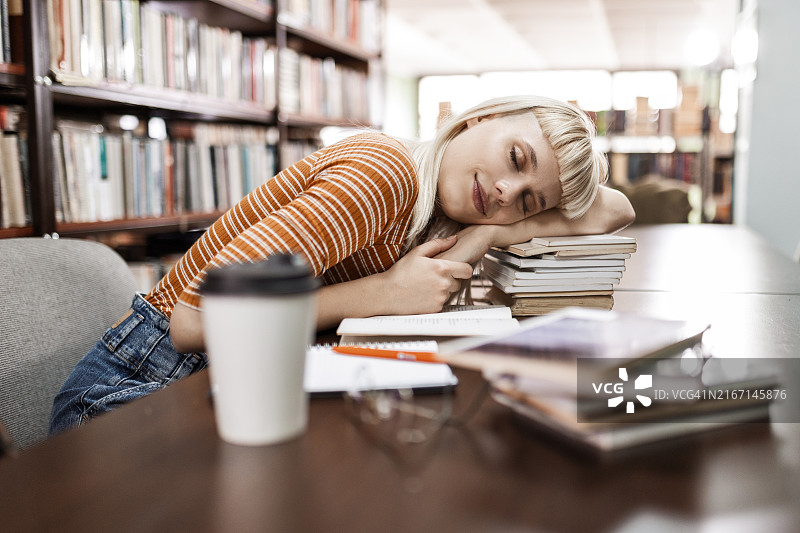 疲惫的女学生在图书馆的书本上睡觉图片素材