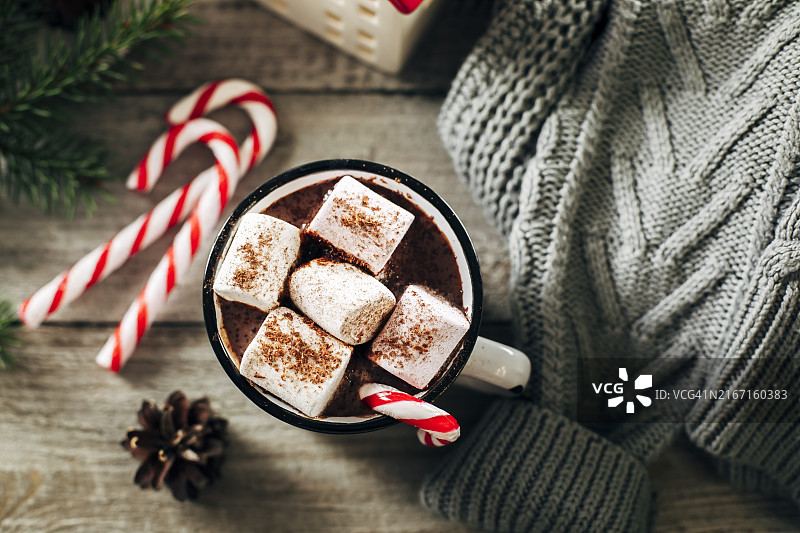 节日马克杯里的热巧克力、棉花糖和拐杖糖，背景是杉树枝和灰色毛衣。图片素材