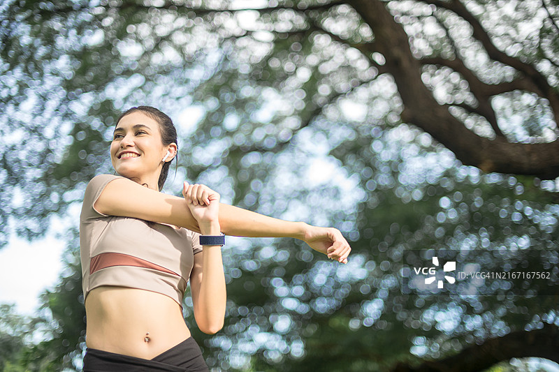 笑容满面的女人在阳光明媚的公园里伸展手臂，穿着运动服和健身追踪器，准备锻炼图片素材