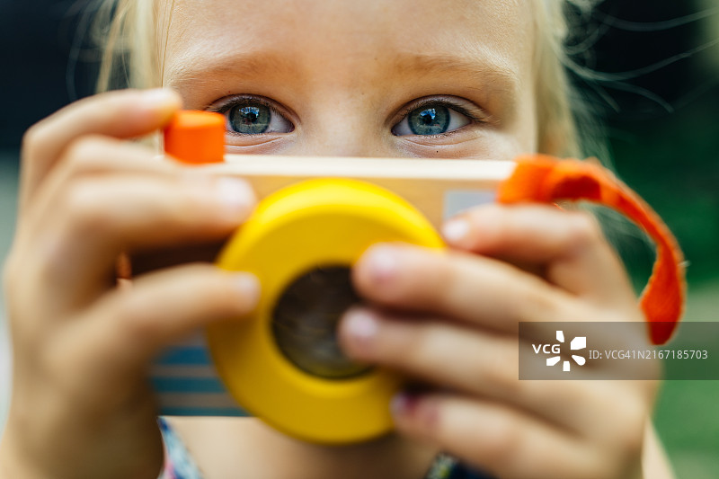 扮演摄影师的可爱小女孩，玩着木制玩具相机图片素材