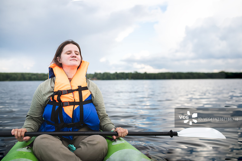 专注当下：中年加大码女性在皮划艇上闭着眼睛，沉浸在大自然和自我意识中图片素材