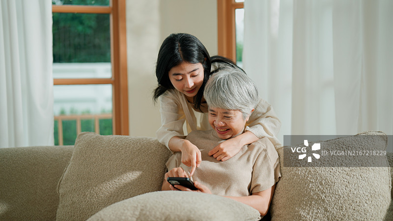 退休的亚洲妇女在家里花时间与女儿一起学习使用新智能手机。图片素材