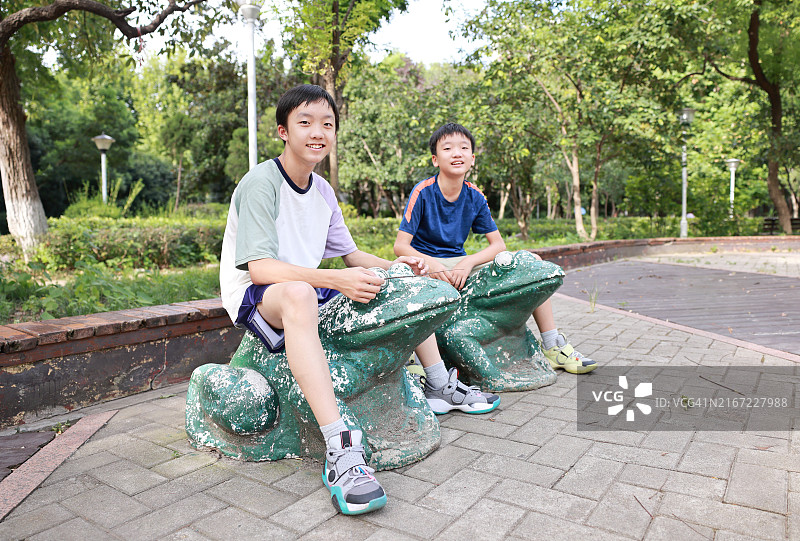 两个男孩坐在青蛙石像上图片素材