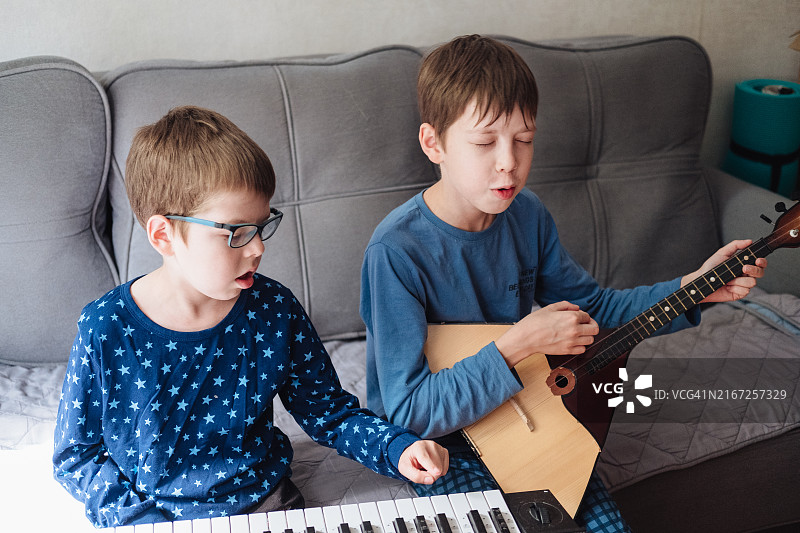 两个男孩在家中沙发上穿着睡衣演奏巴拉莱卡琴和合成器图片素材