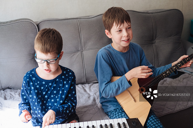 两个男孩在家中沙发上穿着睡衣演奏巴拉莱卡琴和合成器图片素材