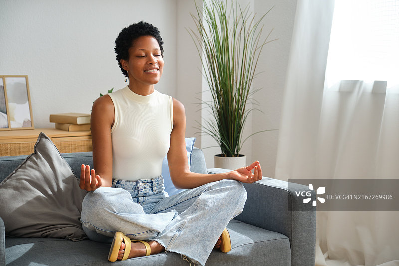 年轻的黑人女性在家中客厅的沙发上冥想图片素材