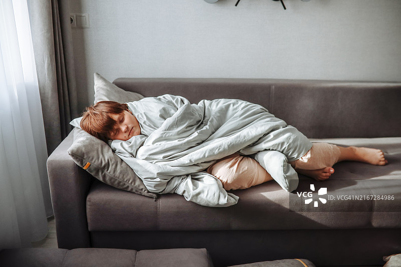 不安的睡眠：躺在客厅沙发上、裹着凌乱毯子的沉迷于逃避现实的少女图片素材