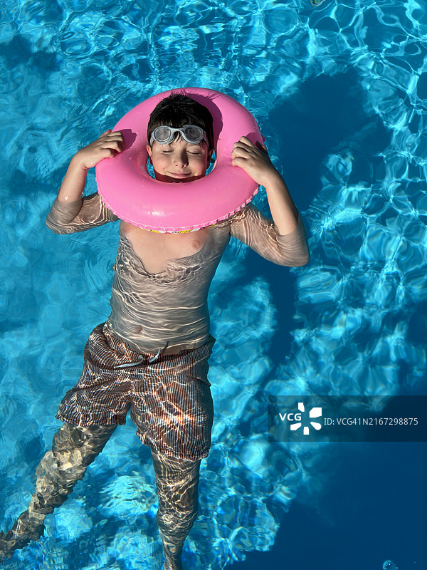 在家庭泳池中漂浮在粉色漂浮物上放松的年轻男孩图片素材