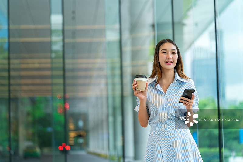 年轻女人在咖啡馆喝咖啡时看窗外，使用手机图片素材