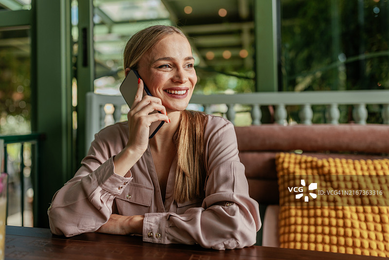 在咖啡馆里用智能手机交谈的微笑女人图片素材