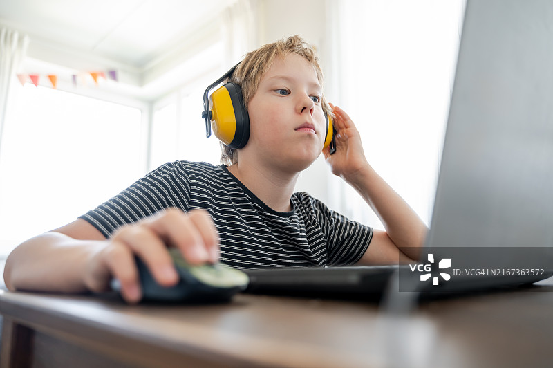 戴降噪耳机玩笔记本电脑的男孩图片素材