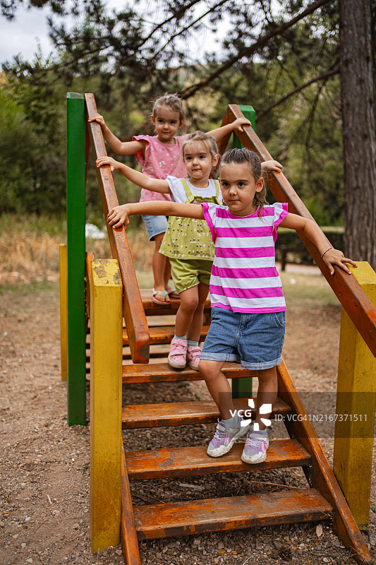 阳光明媚的日子里，母亲在公园里监督她的双胞胎女儿在木制游乐设施上玩耍图片素材