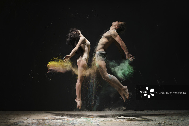 年轻男女在黄色和绿色粉尘云中面对面跳跃图片素材