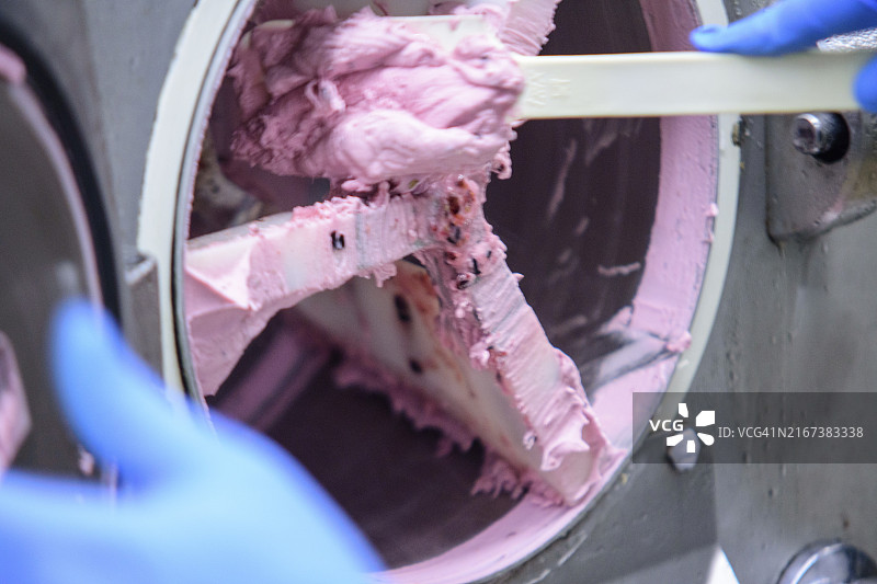 工业工厂中，戴手套的工人在机器上刮粉色冰淇淋，突出搅拌过程图片素材