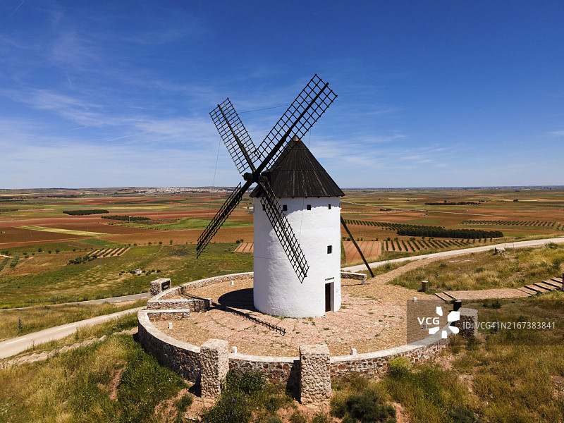 西班牙阿尔卡萨尔德圣胡安山丘上，被石墙和广阔田野环绕的黑色屋顶白色风车，航拍图片素材