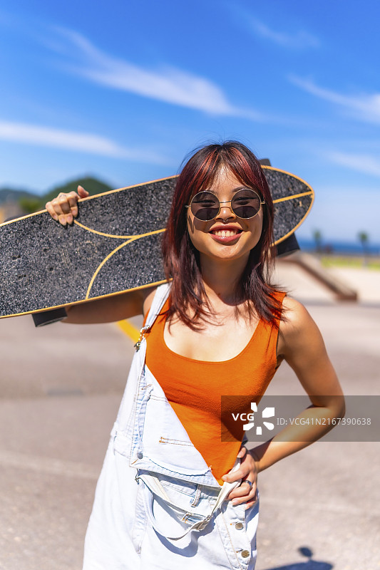 穿着夏装和太阳镜的年轻女子肩扛滑板的竖版照片图片素材
