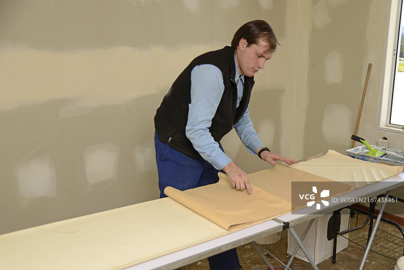 男子卷起一些涂有胶水的壁纸，准备装饰卧室图片素材