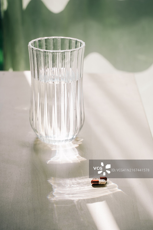 阳光明媚的一天，桌上的一杯水和两粒药丸或补充剂图片素材