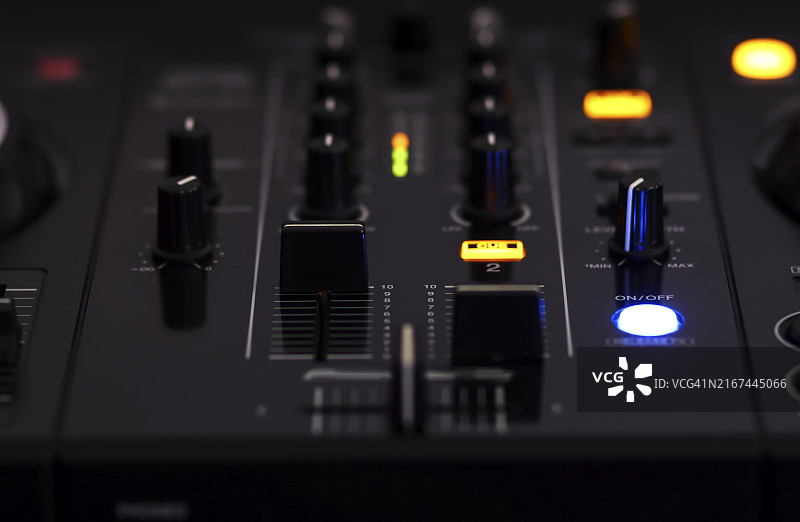 黑暗环境中带有各种旋钮、按钮和发光的灯的音频混音器特写图片素材