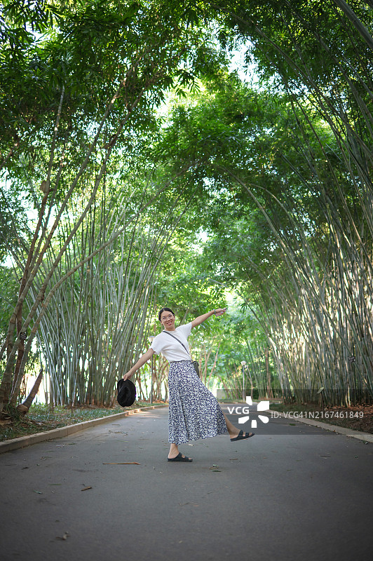 穿着花裙的女人在阳光下竹林小路上嬉戏图片素材