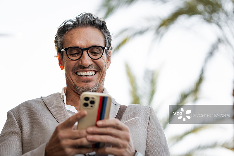 在户外使用手机时大笑的成熟商人图片素材