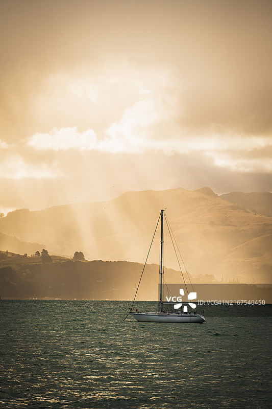 游艇在新西兰阿卡罗阿湾的日落时分停泊，阳光透过云层洒下。图片素材