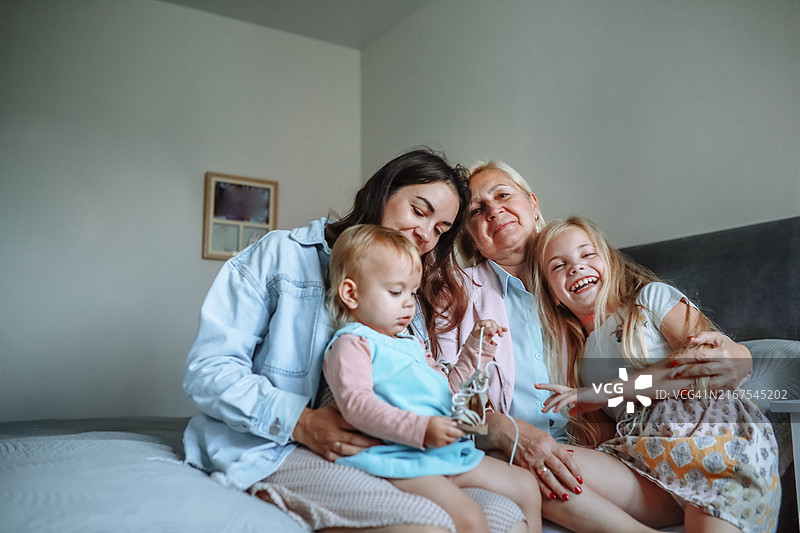 温馨的家庭场景：奶奶、妈妈和两个孩子亲密地坐在温暖卧室的床上图片素材