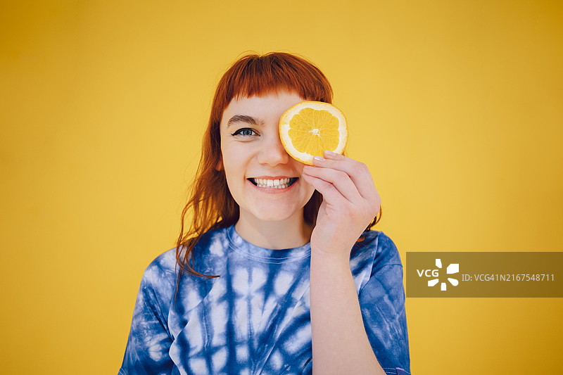 在黄色背景下手持橙子的开朗年轻女人图片素材