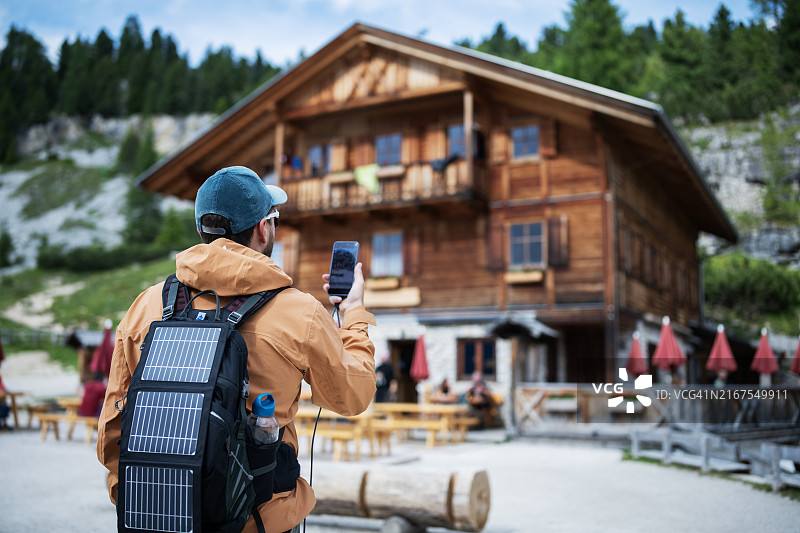 背着便携式太阳能电池板在户外为智能手机充电的男人图片素材