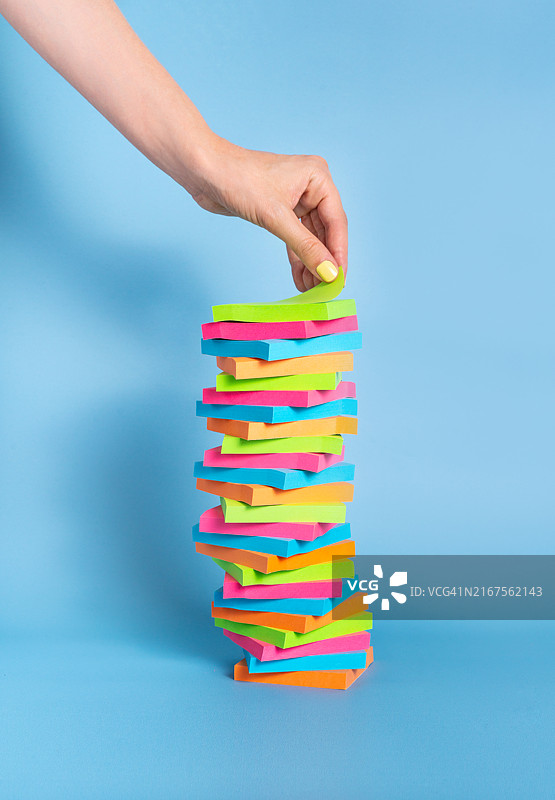 蓝色背景上的便利贴堆叠，手从顶部取下一张图片素材
