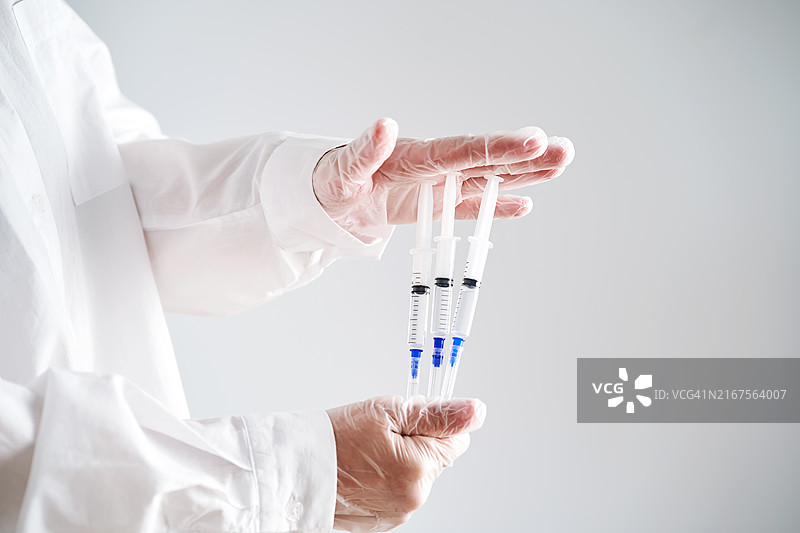 穿着白色外套和戴着手套的医生的手拿着三个装有药物的注射器图片素材