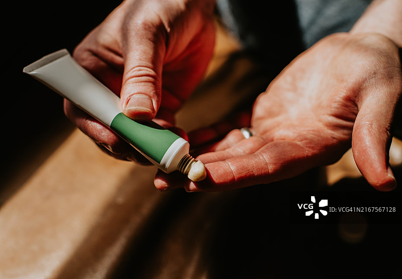 在柔和的光线下，将绿色和白色管中的乳霜涂抹在手掌上的人图片素材