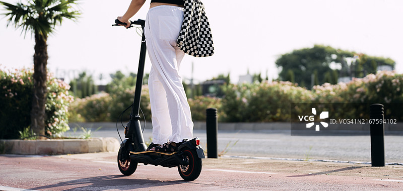 休闲装扮的女人站在街边人行道上骑电动滑板车图片素材