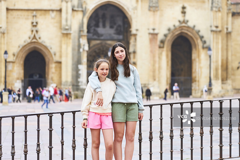 两名游客女孩穿着休闲服站在奥维耶多教堂外，面带微笑地看着镜头的肖像，正面视角图片素材
