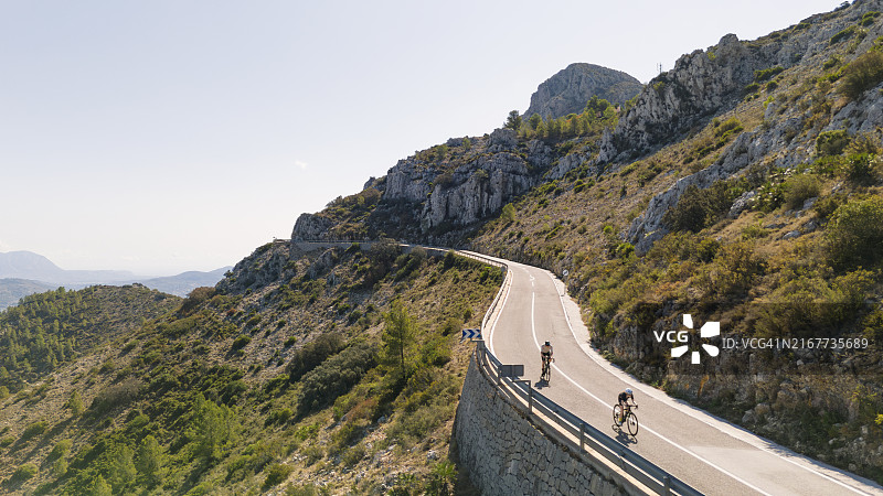 成熟男人和他的十几岁女儿在西班牙山区骑公路自行车的航拍图图片素材