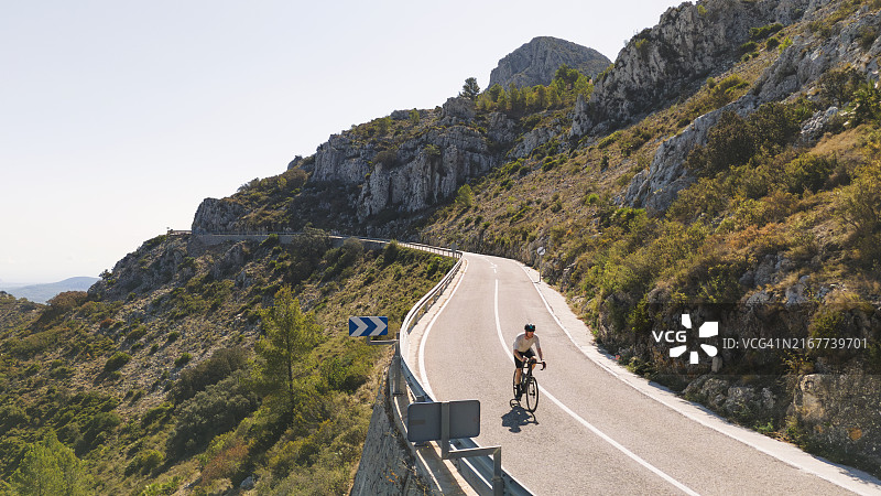 西班牙山区：成熟男人骑公路自行车下坡的无人机正面视角图片素材