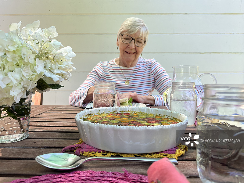 在户外露台上用餐的微笑老年妇女，花瓶里插着鲜花图片素材