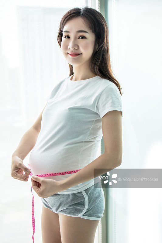 亚裔孕妇用卷尺测量她的腹部图片素材