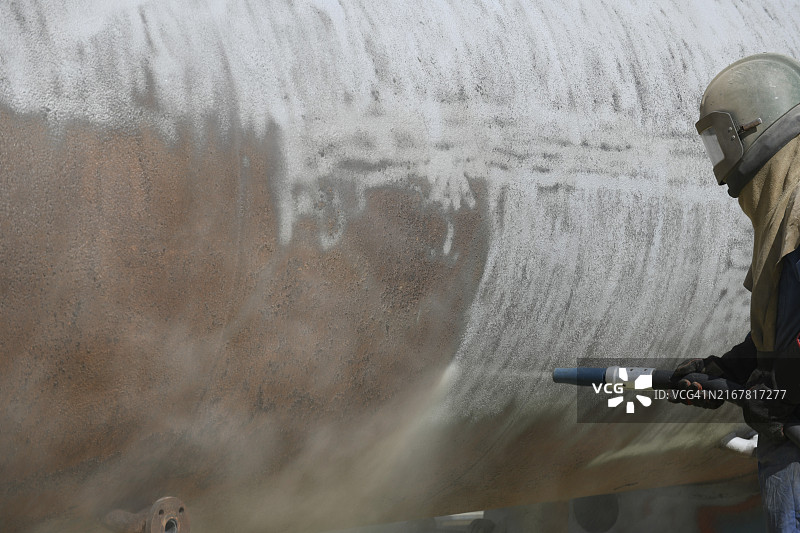 穿着全套安全装备的男人用玻璃砂喷砂处理肉类干燥机的钢制外壳图片素材