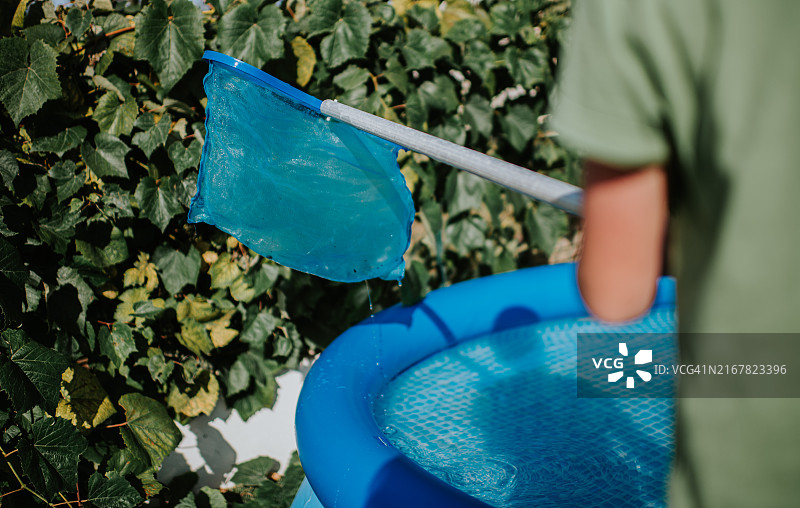 儿童手持泳池网兜在充气泳池旁图片素材