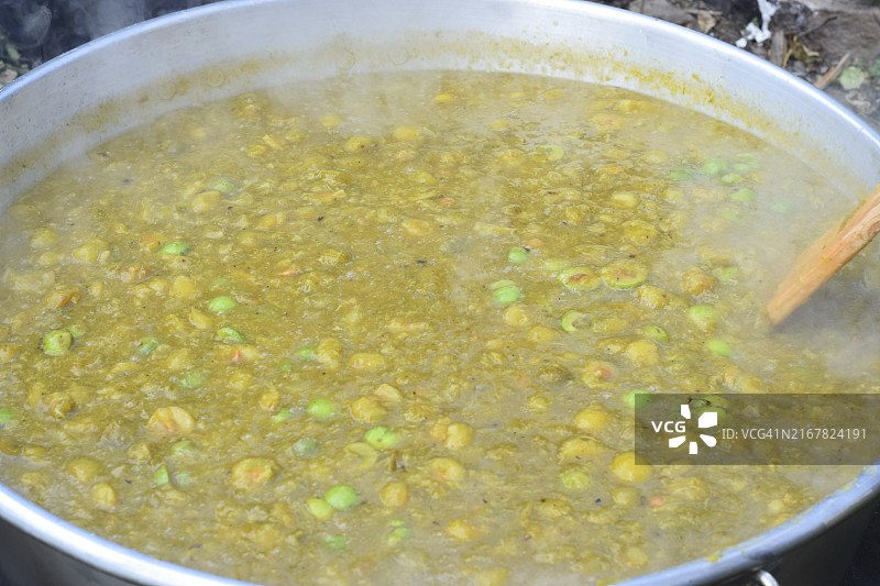 在户外烹饪的大锅炖菜，蒸汽袅袅，配有木勺图片素材