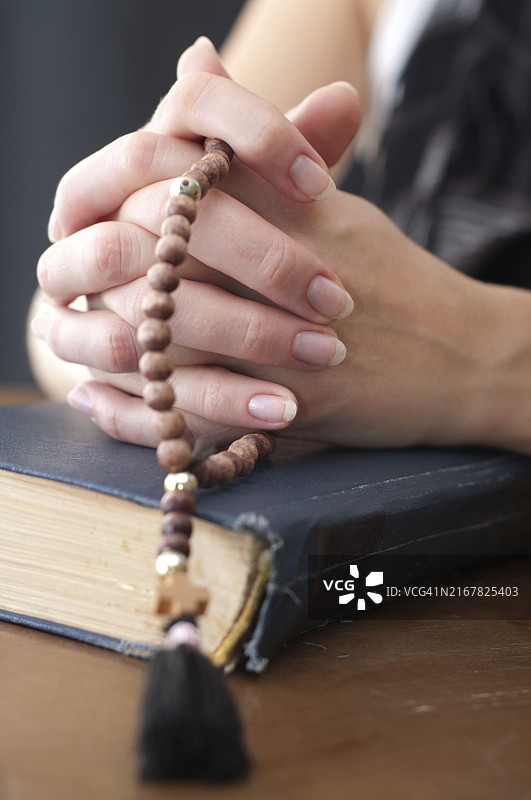 女人手拿着念珠和蓝色圣经祈祷，浅景深对焦于手部图片素材