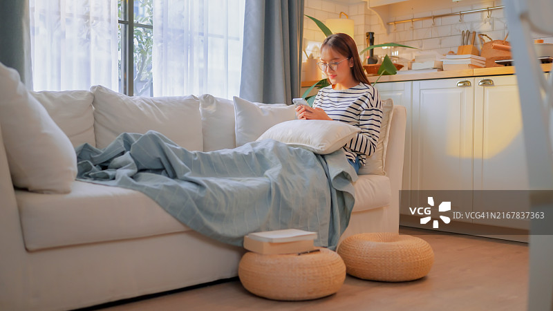 亚洲女人在沙发上使用智能手机放松图片素材