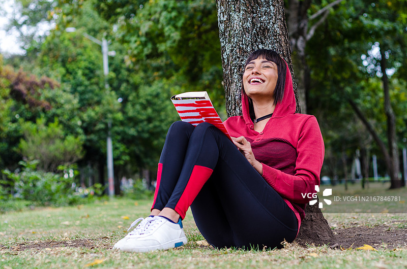 美丽的年轻女性在公园的户外阅读一本书图片素材
