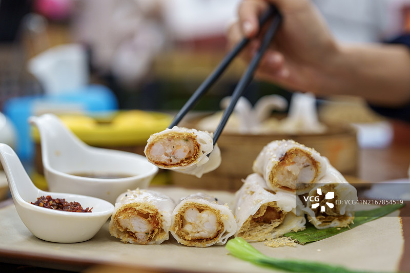 年轻的亚洲女性用筷子享用点心，中餐厅的桌子上摆着各种新鲜菜肴的局部照片图片素材