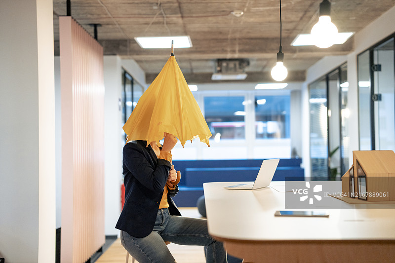 年轻女商人坐在办公室的办公桌旁，撑着雨伞图片素材