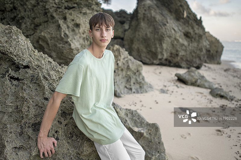倚靠在海滩岩石上的少年肖像图片素材