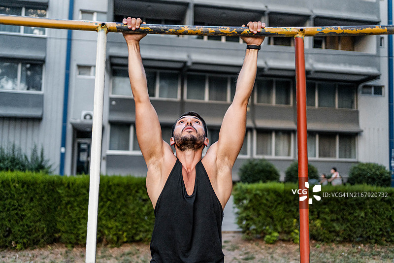 在户外单杠上做引体向上的健身男人图片素材