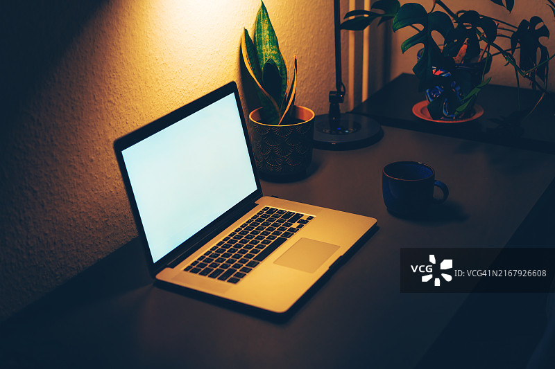 夜晚桌子上带有空白屏幕的笔记本电脑图片素材